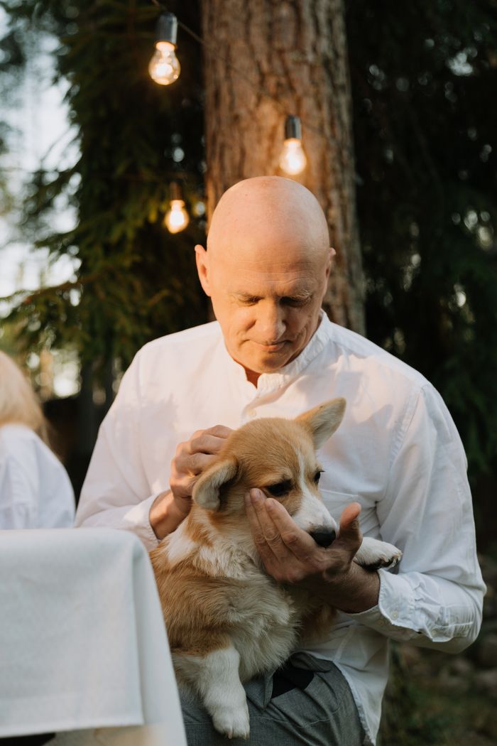 Mastering the First Impression: Your intriguing post title goes here A bald man gently cradles a corgi dog in his arms outdoors during the day.